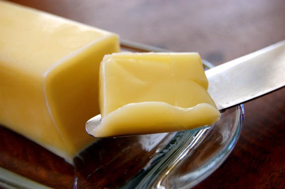 A piece of butter on a glass plate with a knife.