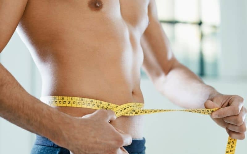 A man measuring his waistline with a measuring tape.