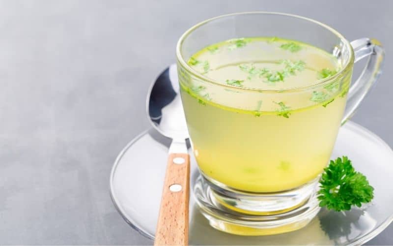 A yellow liquid with garnish in a clear mug.