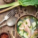 Soup in a pot with spoon and fork on a wooden surface.