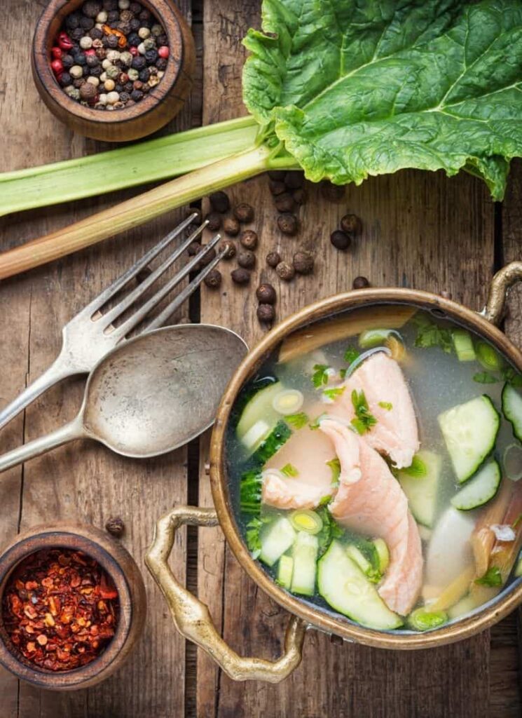 Soup in a pot with spoon and fork on a wooden surface.