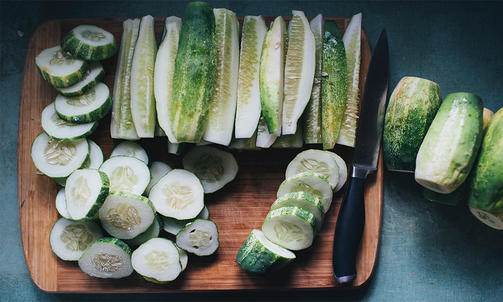 Cucumbers being sliced with a knife on a cutting board for a ketogenic diet.