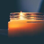 A tallow candle is lit on a table in front of a dark background.