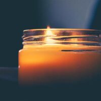 A tallow candle is lit on a table in front of a dark background.