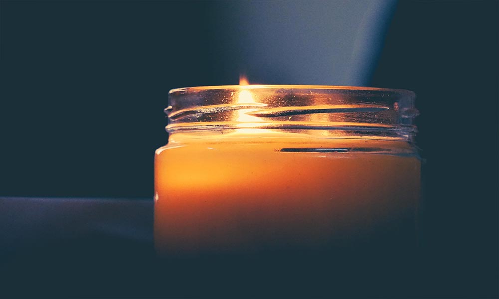 A tallow candle is lit on a table in front of a dark background.