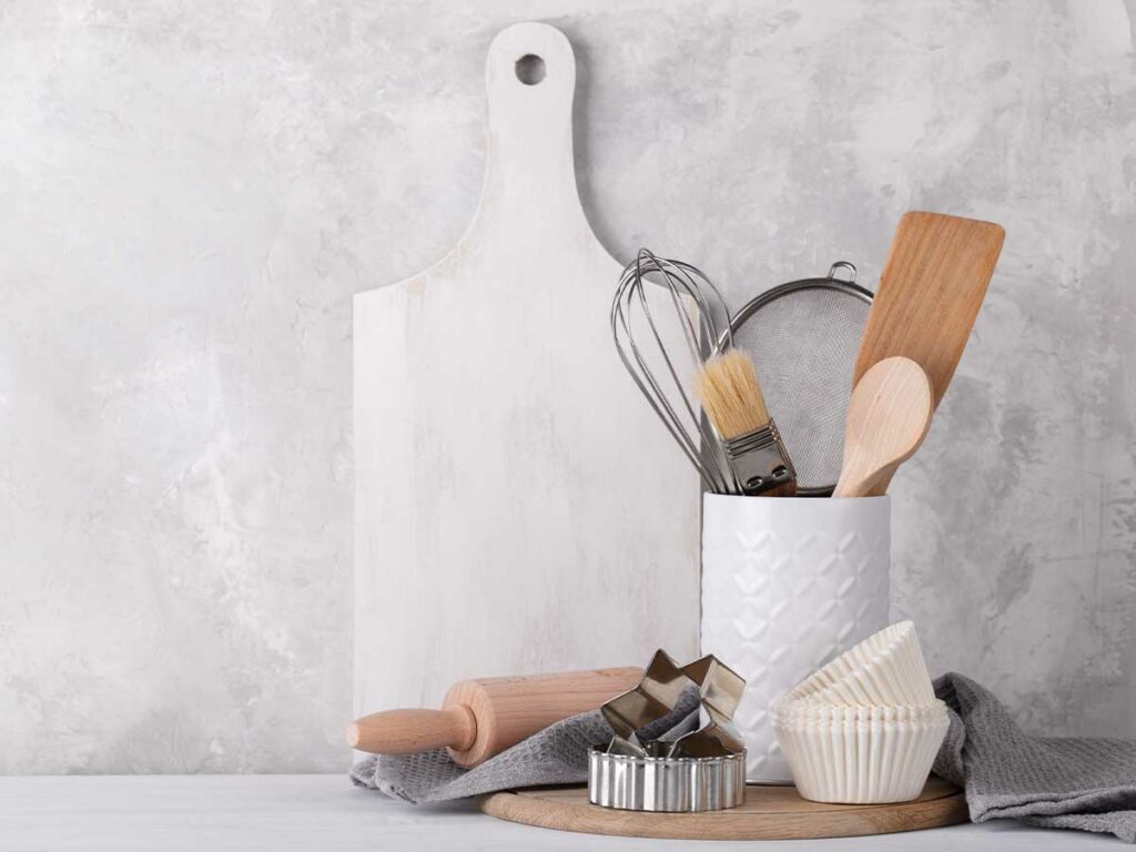 White kitchen tools and a cutting board on a concrete wall.