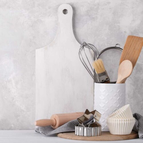 White kitchen tools and a cutting board on a concrete wall.