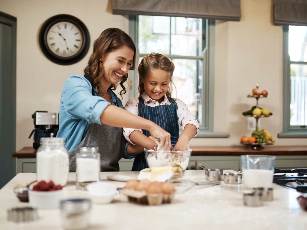 A mother and daughter using kitchen tools to prepare food in the kitchen.