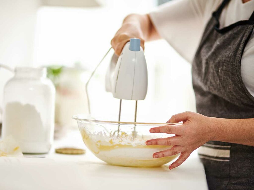 A woman mixing ingredients in a bowl with an electric mixer.