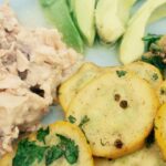 Salmon, avocado and slices of potatoes on a white surface.