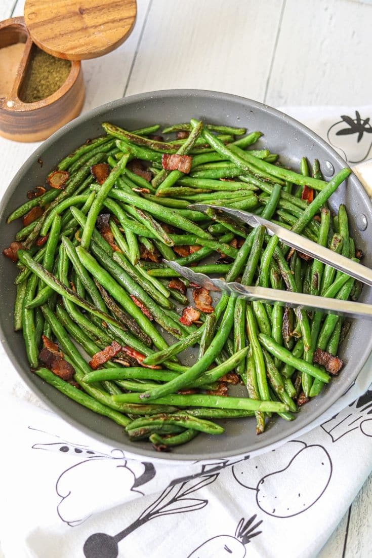 Sautéed green bean in a pan on a white surface.