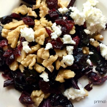 A plate with beet greens, cranberries, nuts and feta cheese.