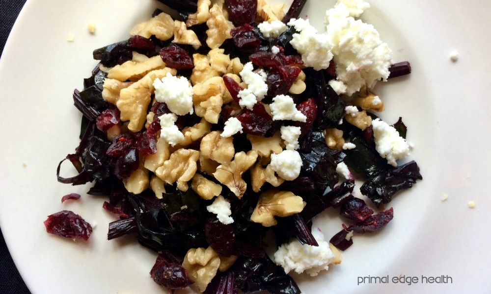 A plate with beet greens, cranberries, nuts and feta cheese.