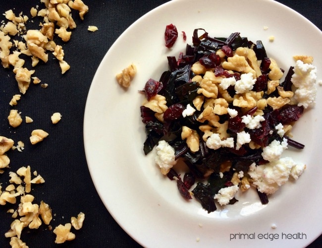 A white plate of beet greens salad with walnuts, cranberries and cheese.