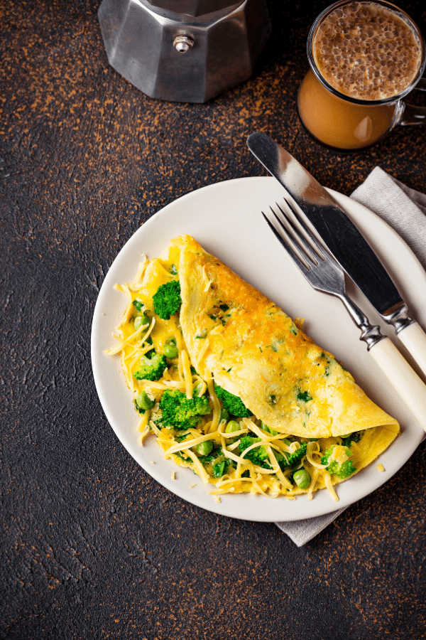 Omelette with broccoli and cheese on a plate with fork and knife.