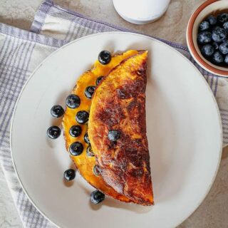 Sweet omelette on a white plate served with blueberries.