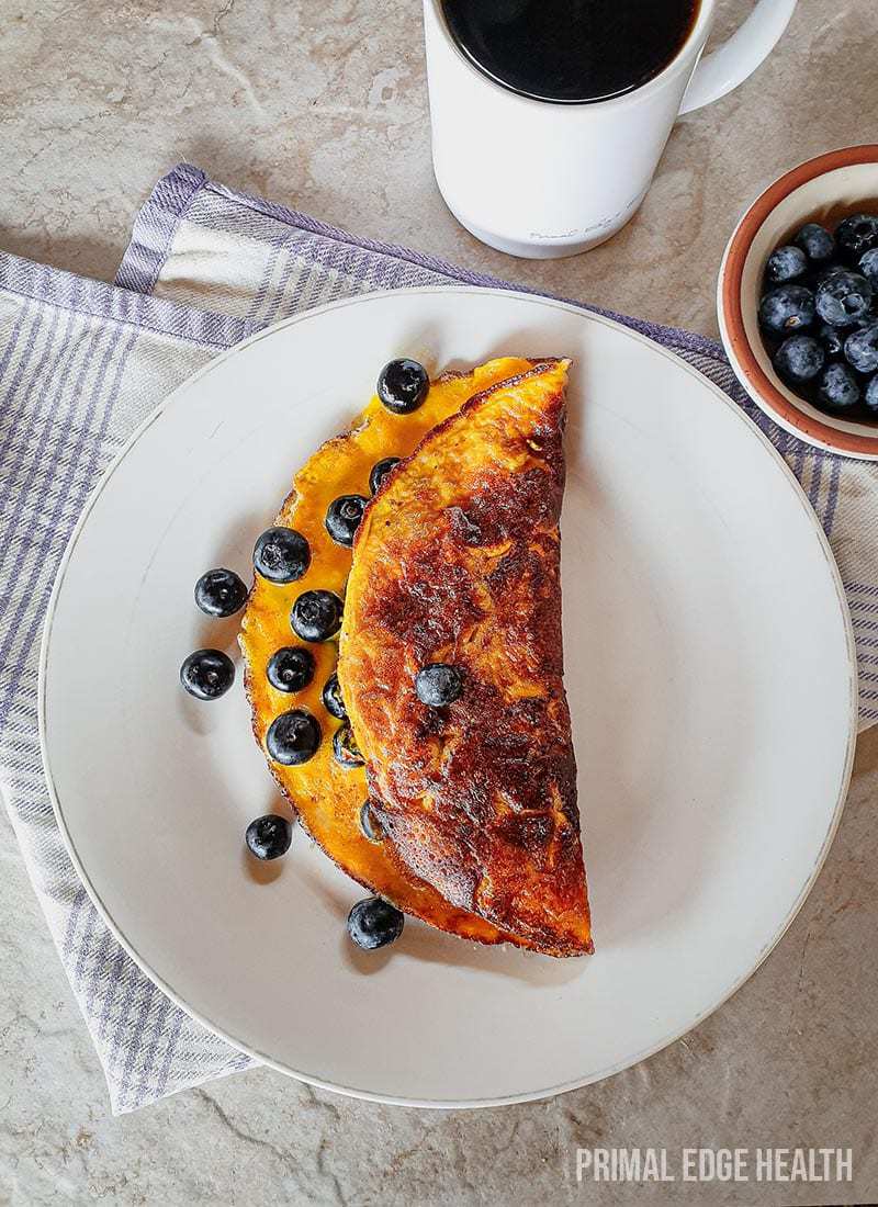 Sweet omelette on a white plate served with blueberries.