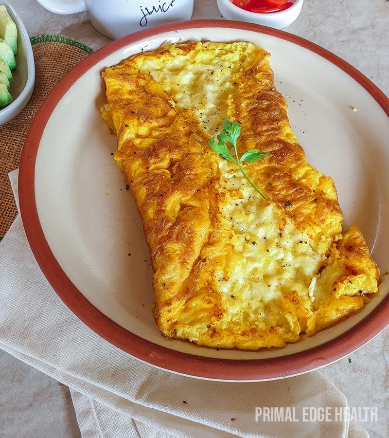 A plate of three cheese omelette with garnish on a white surface.