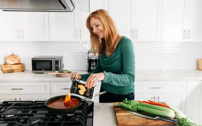 A woman wearing green cooking using kettle and fire bone broth.