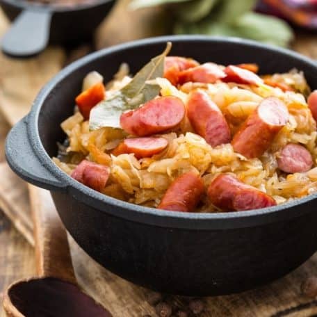 Cabbage and sausage stir fry in a black pot on a wooden surface.