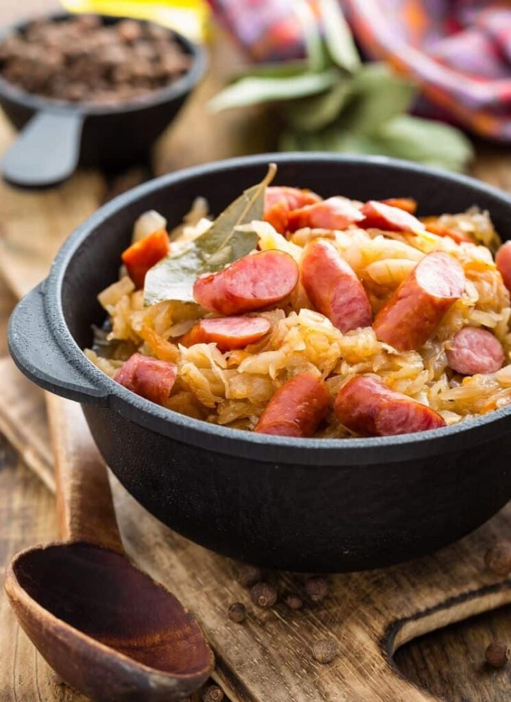 Cabbage and sausage stir fry in a black pot on a wooden surface.