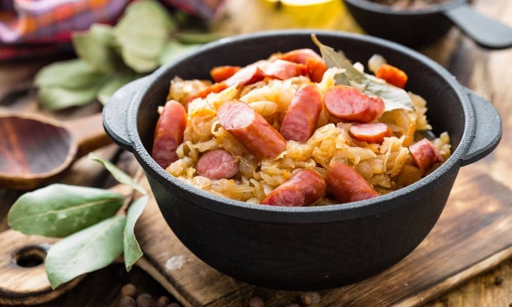 A black pot containing breakfast sausage and cabbage.