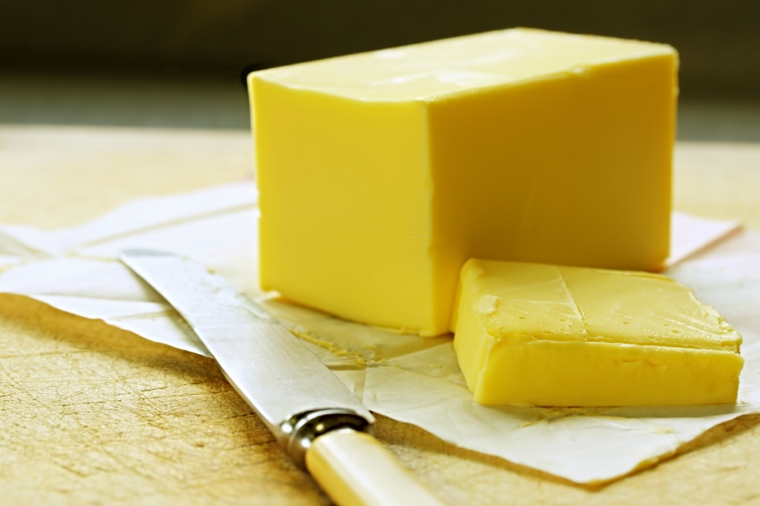 A stick of butter with a sliced piece of it on the side.