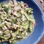 Zoodles with tuna and pine nuts on a blue plate.