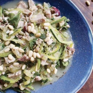 Zoodles with tuna and pine nuts on a blue plate.