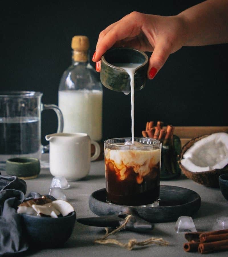 Cream being poured in a glass of brown liquid.