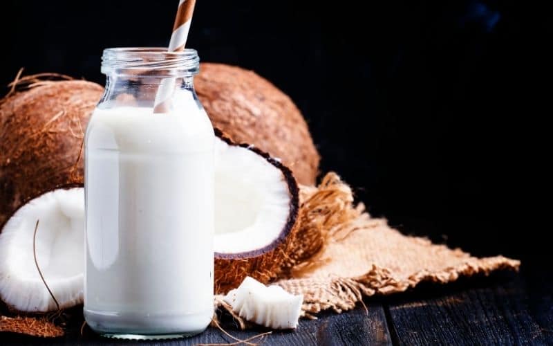 A bottle of coconut milk surrounded by coconuts.