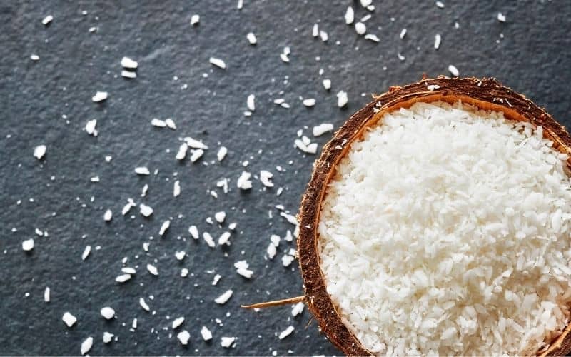 Shredded coconut in a coconut shell on a grey surface.