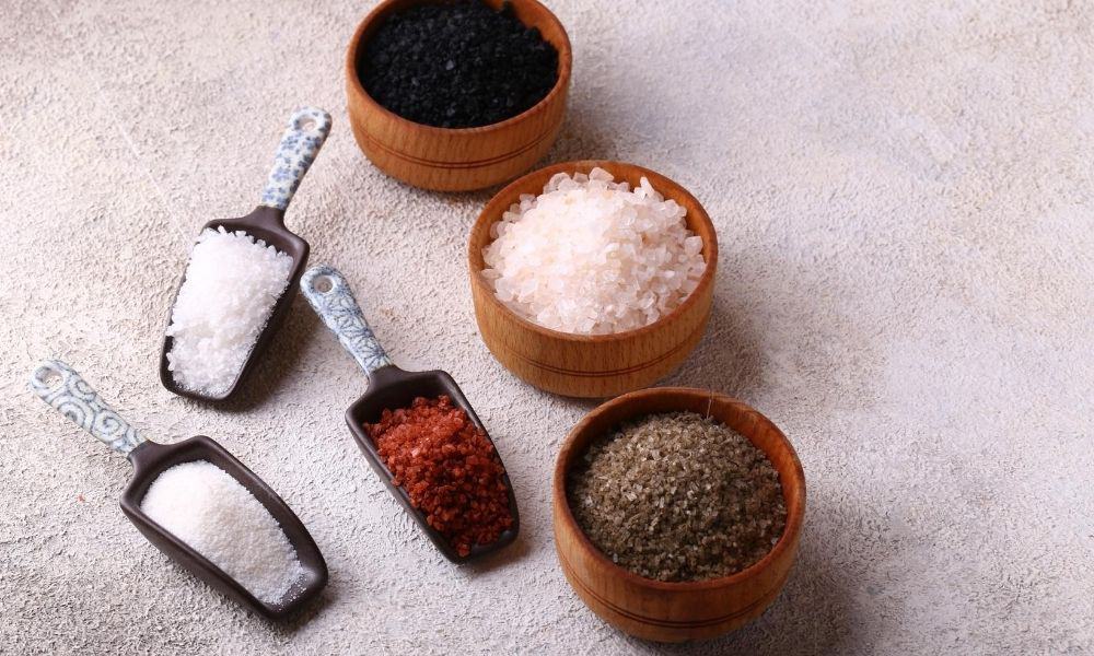 Various types of salt in bowls and scoops.