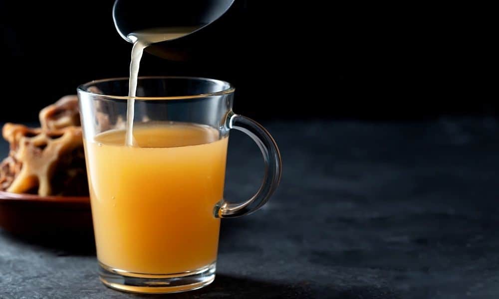 Ladle pouring a brown liquid in a clear mug.