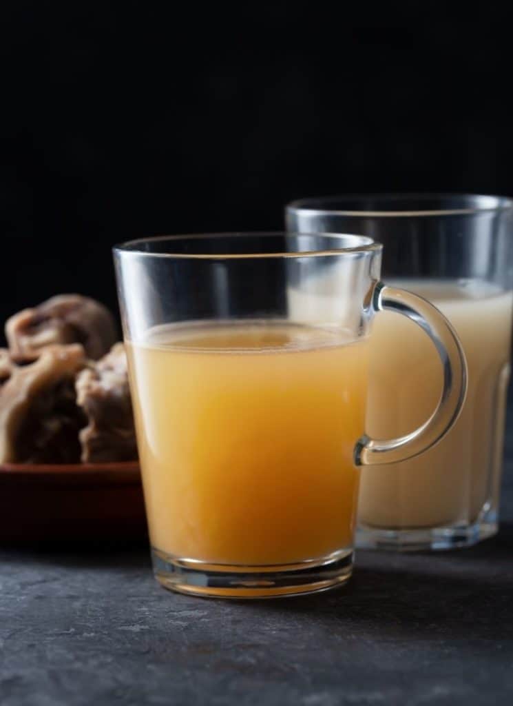 Two glasses of bone broth on a grey surface.
