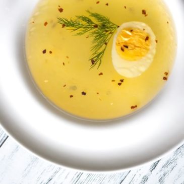 Yellow soup with egg in a white bowl on a white wooden surface.
