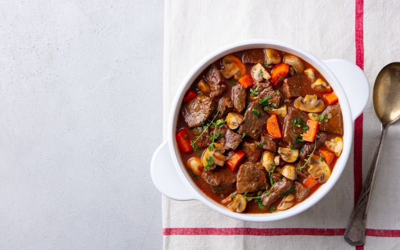 Beef stew in a white bowl with bone broth, carrots, and mushrooms.