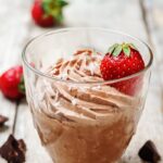 Keto chocolate mousse in a glass with strawberry on a wooden surface.