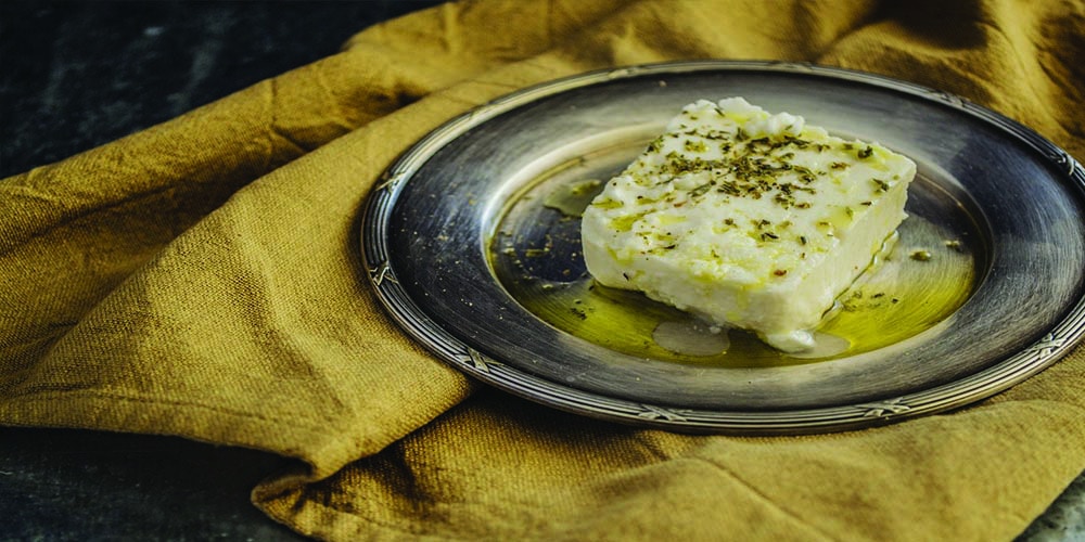 A plate of cheese with herbs garnish.
