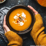 A person's hands holding a bowl of low-carb pumpkin soup.