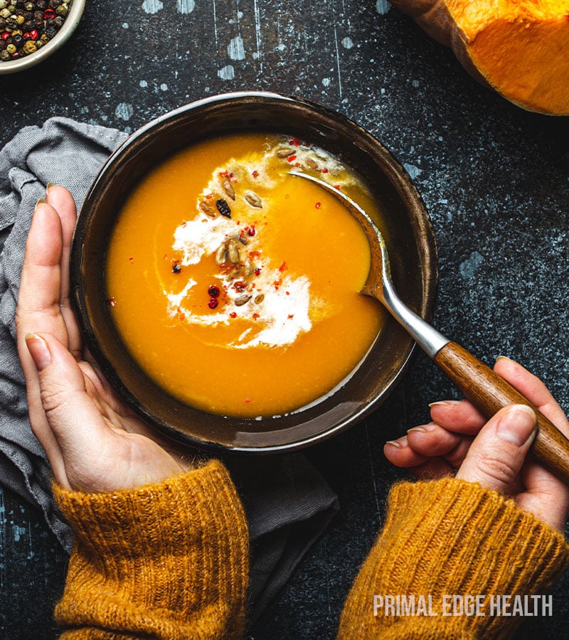 A person's hand holding a bowl of low-carb pumpkin soup and spoon with the other.