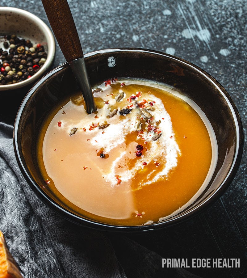 Low-carb pumpkin soup in a black bowl served with a spoon.