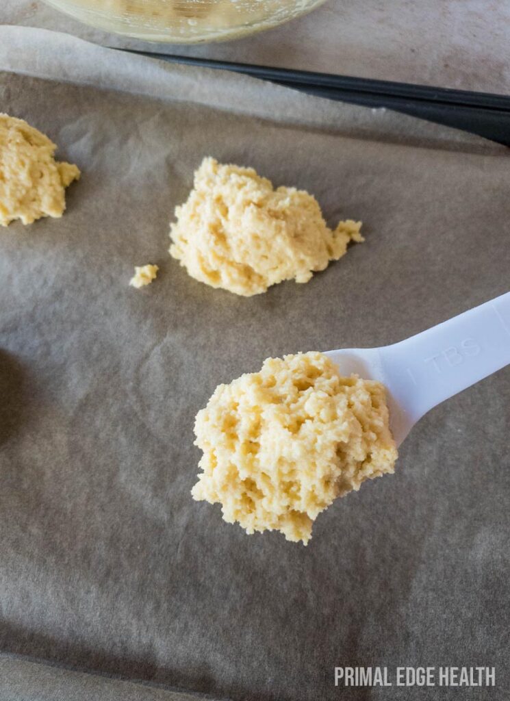 Portioning drop biscuits dough on a baking sheet with a white spoon.