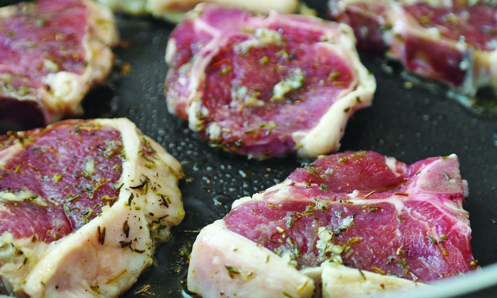 Meat slices with herb garnish being cooked in a pan.