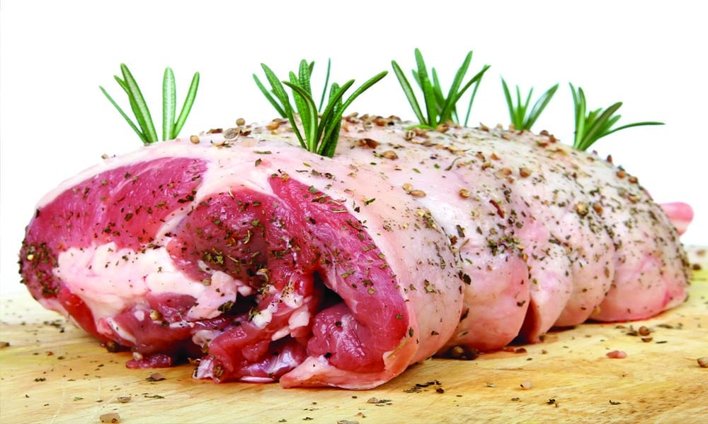 A slab of meat garnished with herbs sitting on a wooden board.