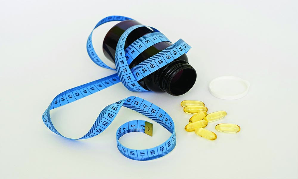 A blue tape measure tied to a brown bottle of supplement with pills coming out of it.