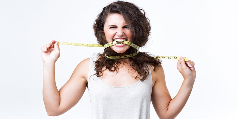 A woman with tape measure tied to her head and biting a part of it.