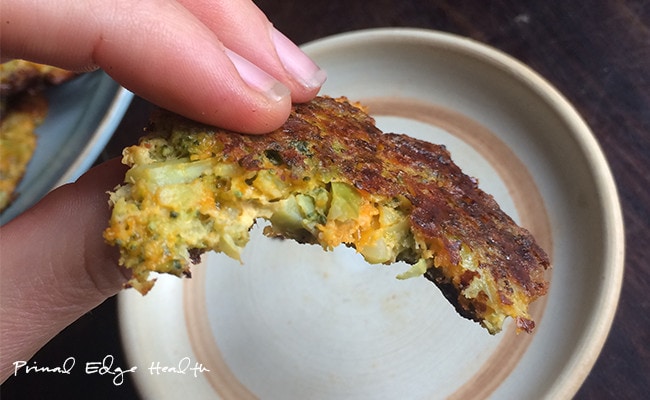 A hand holding a piece of low-carb broccoli fritters with a bite.