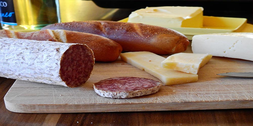 Different types of sausages and cheese on a wooden chopping board.