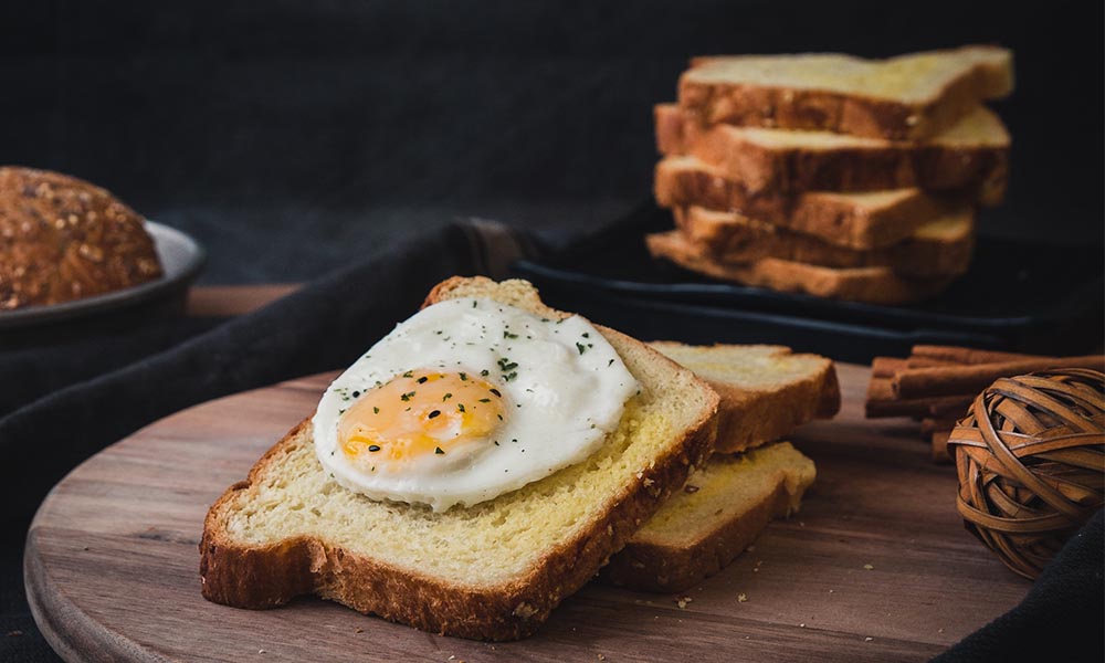 Slices of keto bread on a stack on a wooden board with fried egg on top of one of the slices.